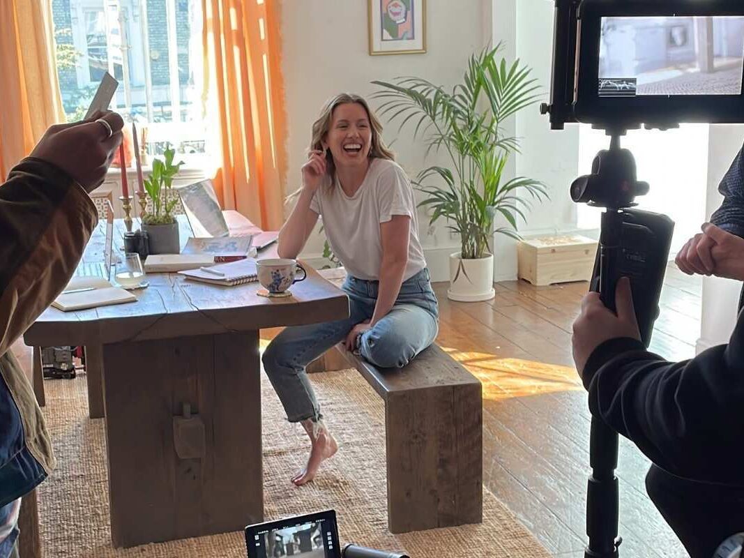 An actor sits in a stylish dining room, smiling at the film crew.