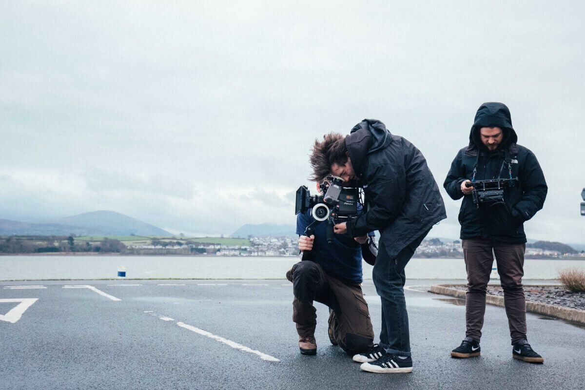 The STORM + SHELTER team leaning over a camera on an open road with mountains in the distance.
